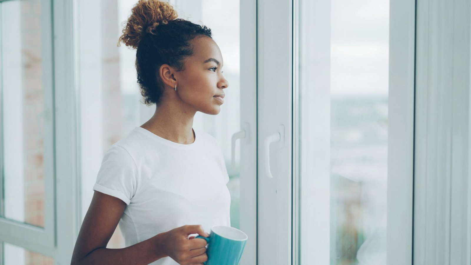 Mujer con una taza mirando por la ventana con calma